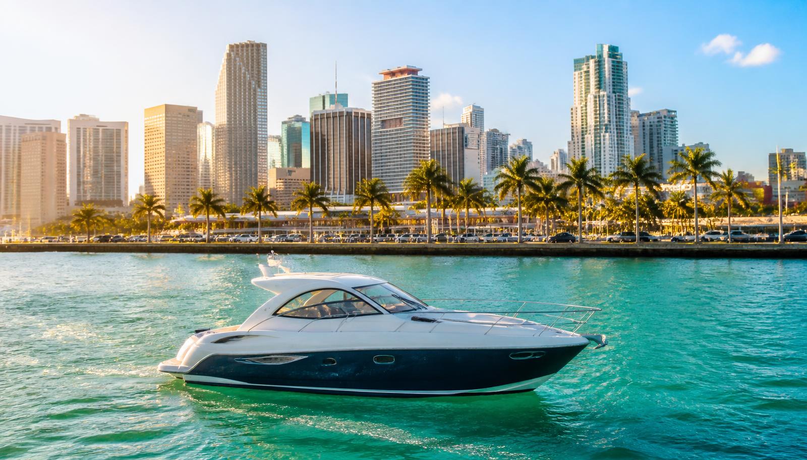 A small white motor yacht on turquoise Biscayne Bay water with the downtown Miami skyline and palm-lined causeway behind