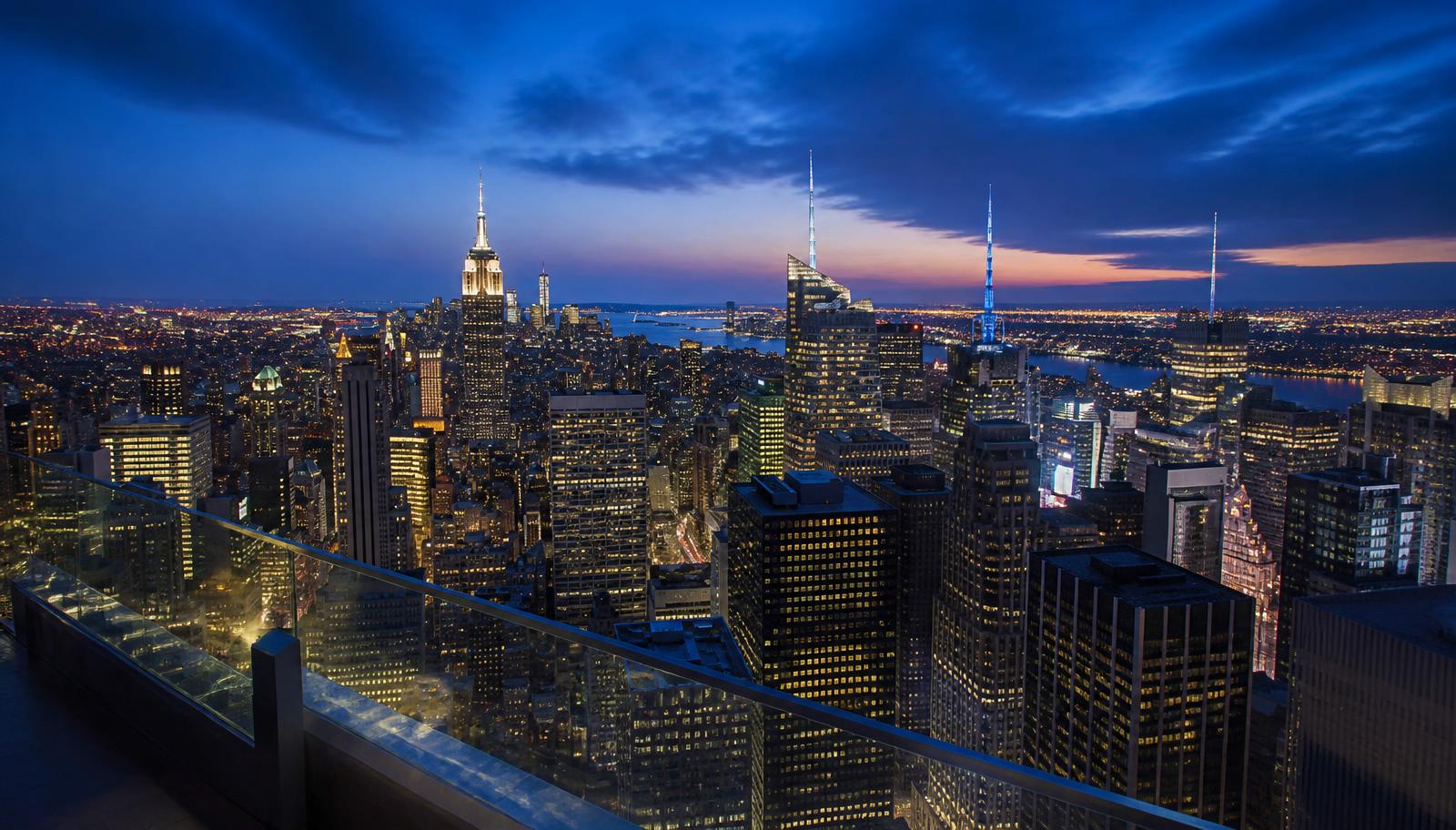 Midtown Manhattan skyline at blue hour seen over the glass railing of a high observation deck